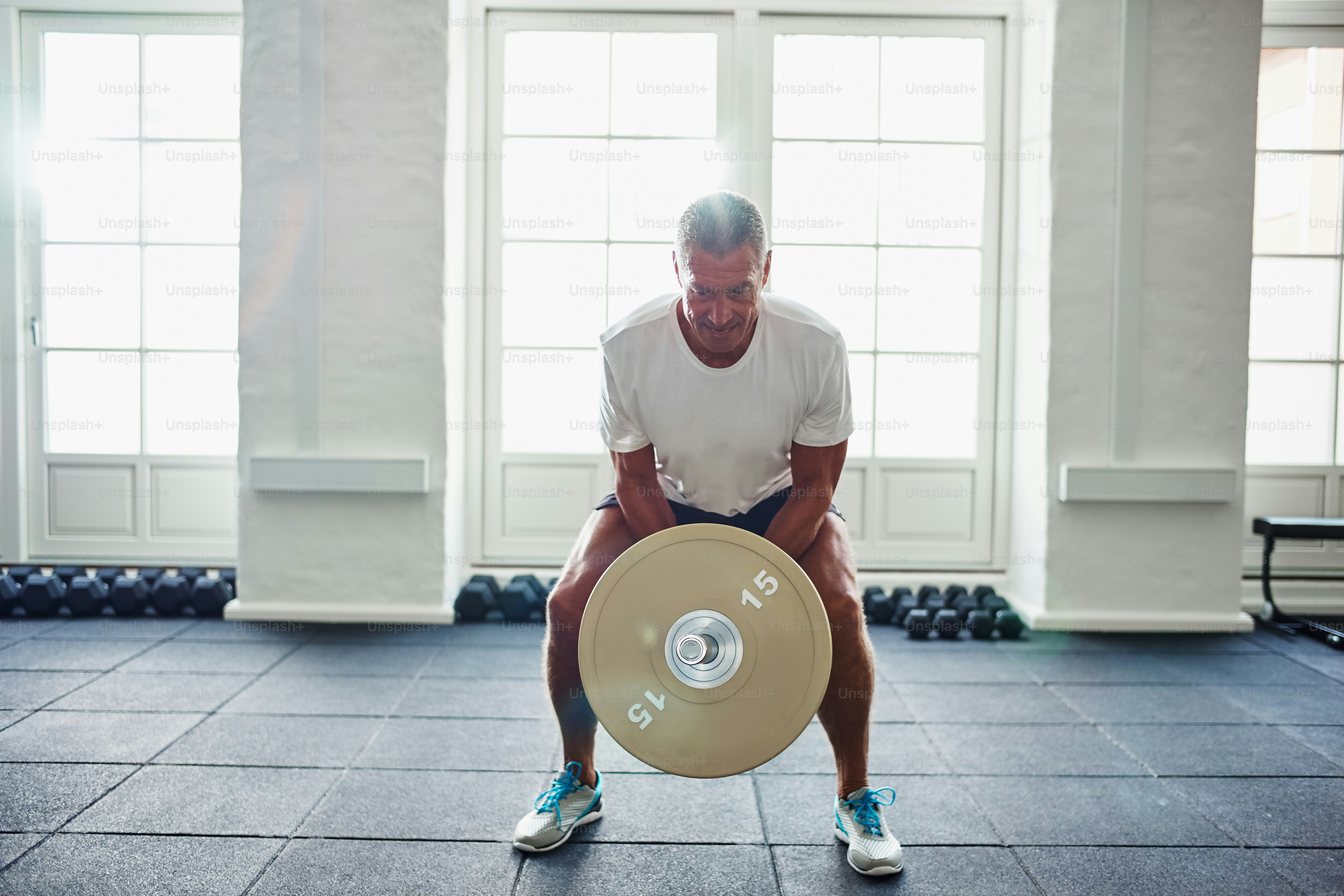 Mature man in sportswear standing alone in a gym focused on lifting weights during a workout