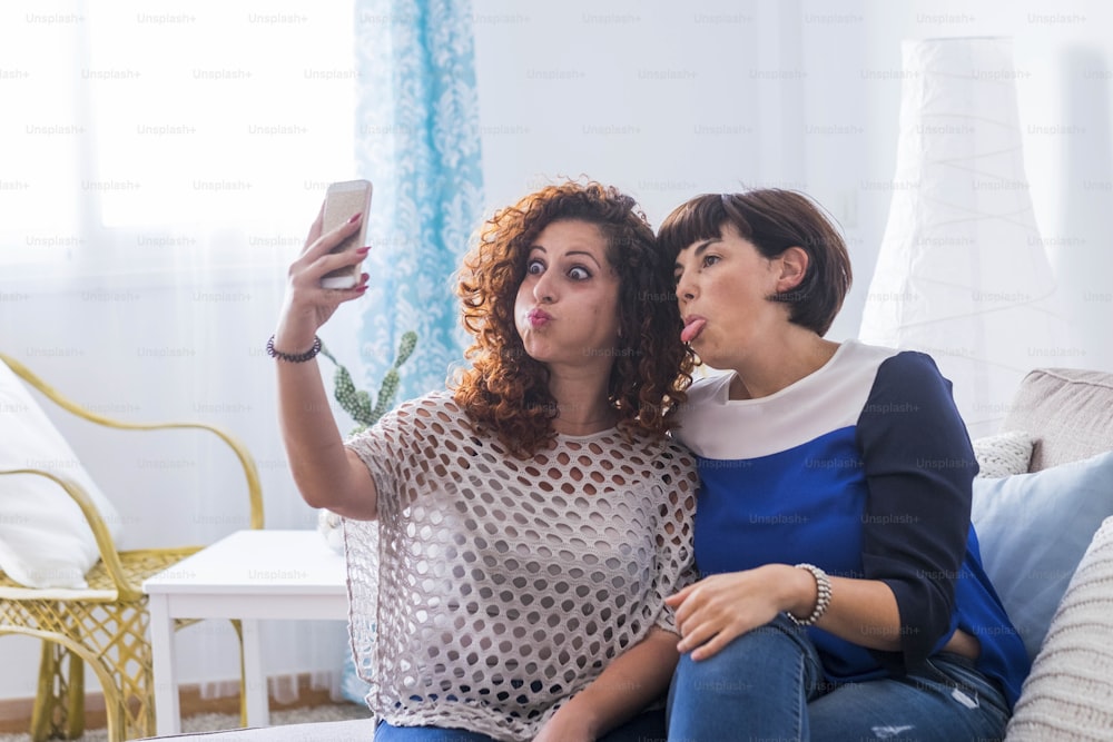 two young women taking pictures with mobile phone at home doing nice and funny expressions. best friends that love to communicate on the net with friends.