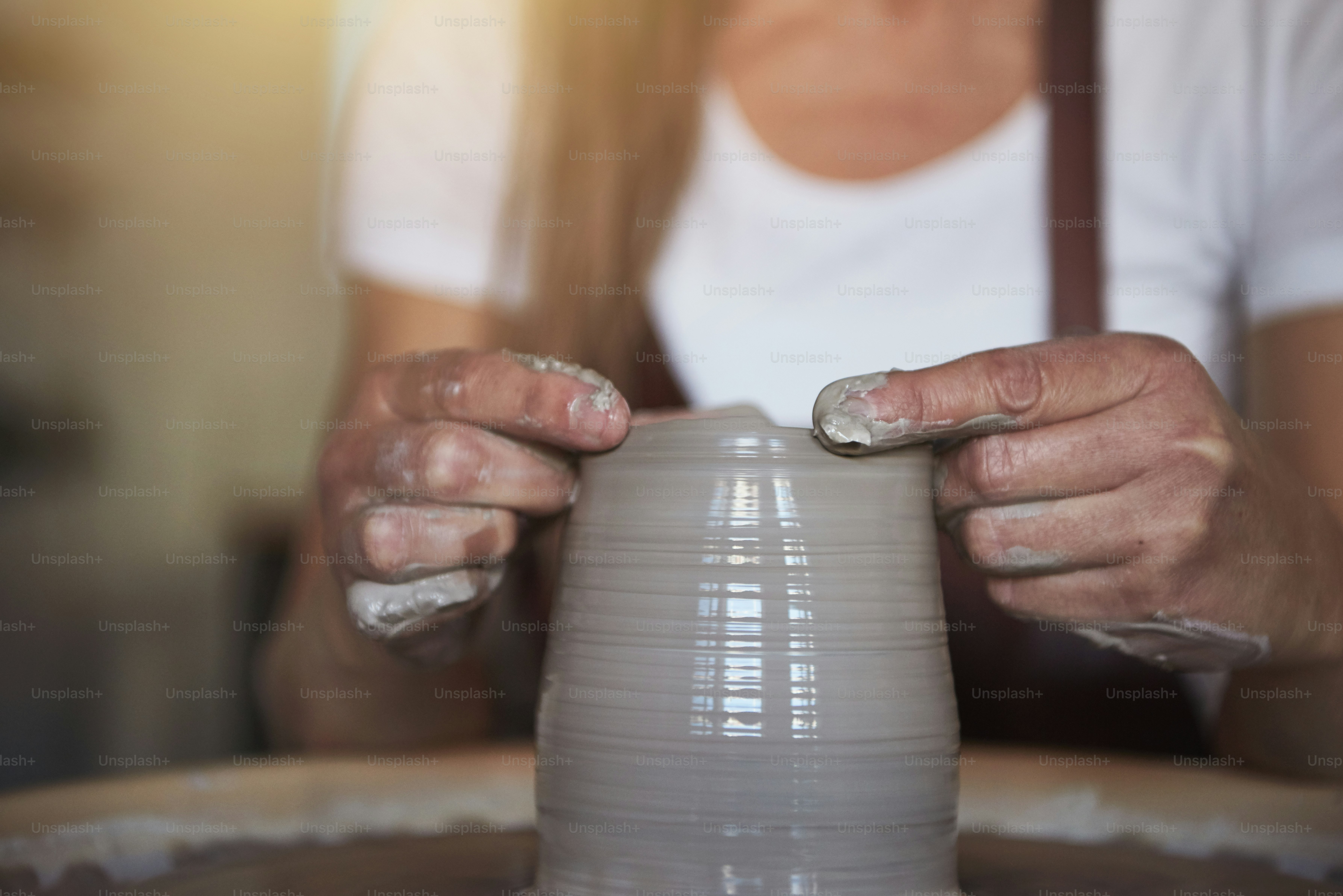 Creative artisan shaping wet clay with her hands on a pottery wheel while sitting in her ceramic