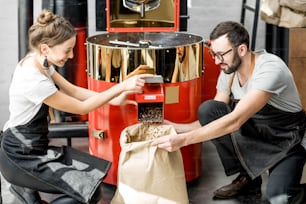 Couple pouring roasted coffee beans into the paper bag from the roaster machine for selling