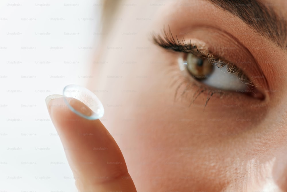Kontaktlinse für das Sehen. Nahaufnahme des weiblichen Auges mit Kontaktlinse auf ihre braunen Augen. Schöne Frau, die Augenlinsen mit den Händen setzt. Opthalmologie Medizin und Gesundheit. Hohe Auflösung