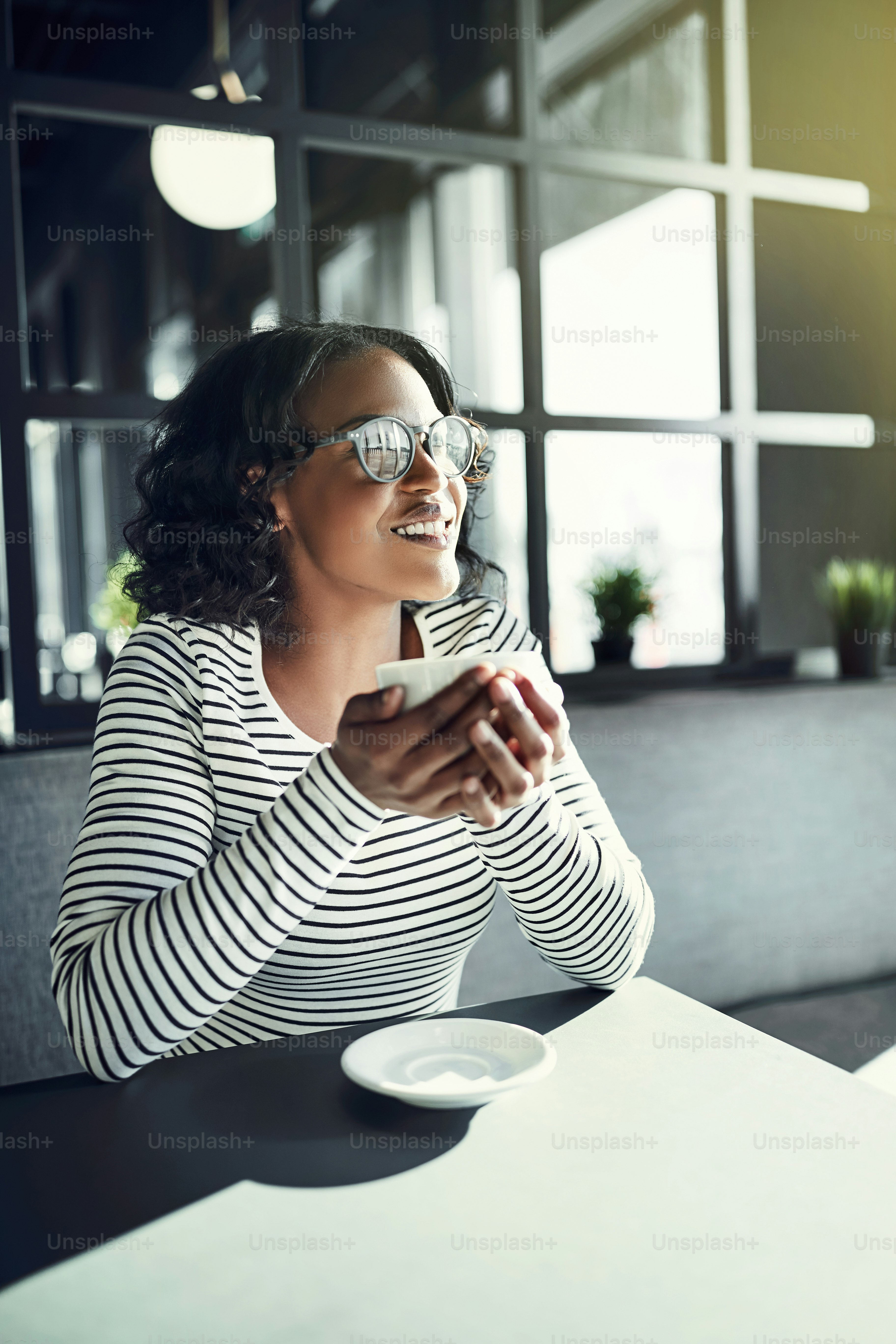 Smiling young African woman sitting at a table in a cafe looking out the window while enjoying a fresh cup of coffee