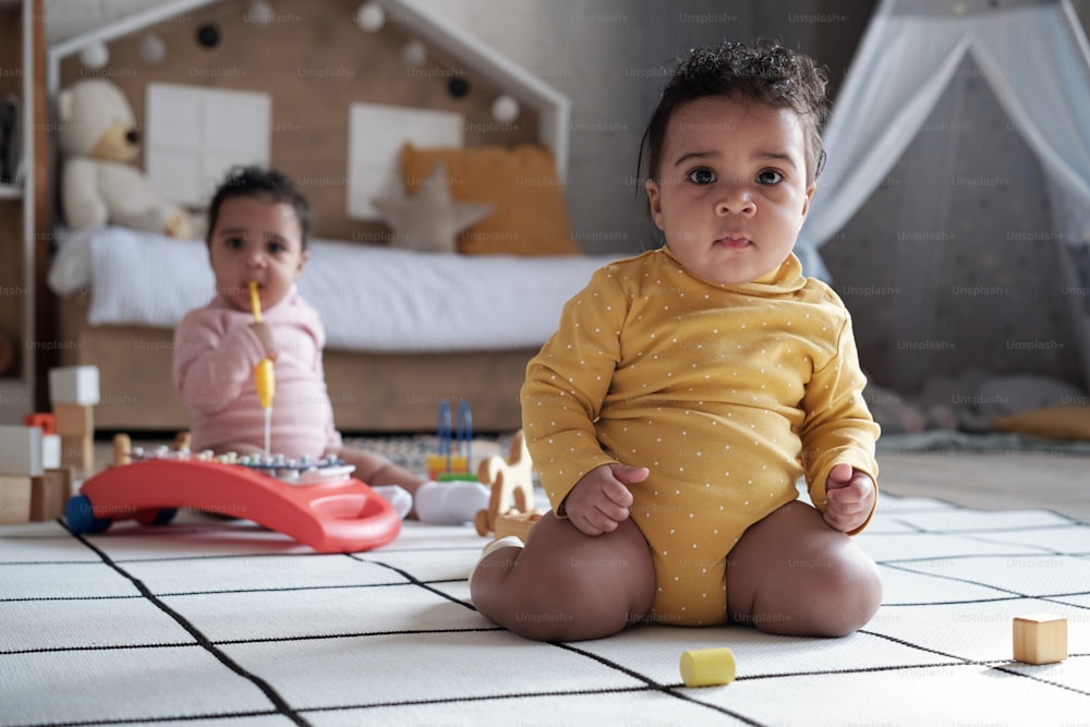 Colpo di messa a fuoco selettiva di due adorabili bambini gemelli seduti sul pavimento nella stanza dei bambini del soppalco che guardano la fotocamera