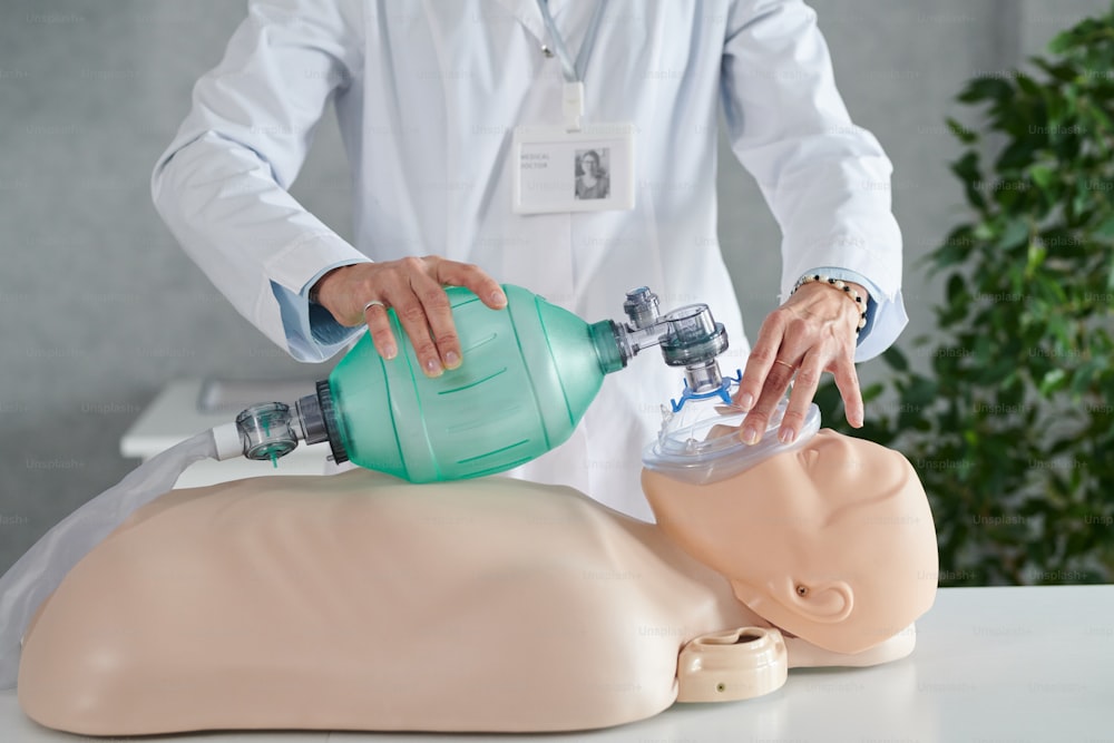 Primo piano dell'operatore medico in camice bianco che dimostra la rianimazione del paziente sul manichino con la maschera dell'ossigeno