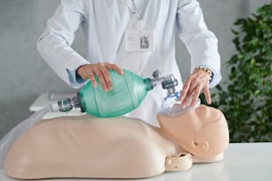 Nahaufnahme eines medizinischen Mitarbeiters im weißen Kittel, der die Reanimation des Patienten auf einer Schaufensterpuppe mit Sauerstoffmaske demonstriert
