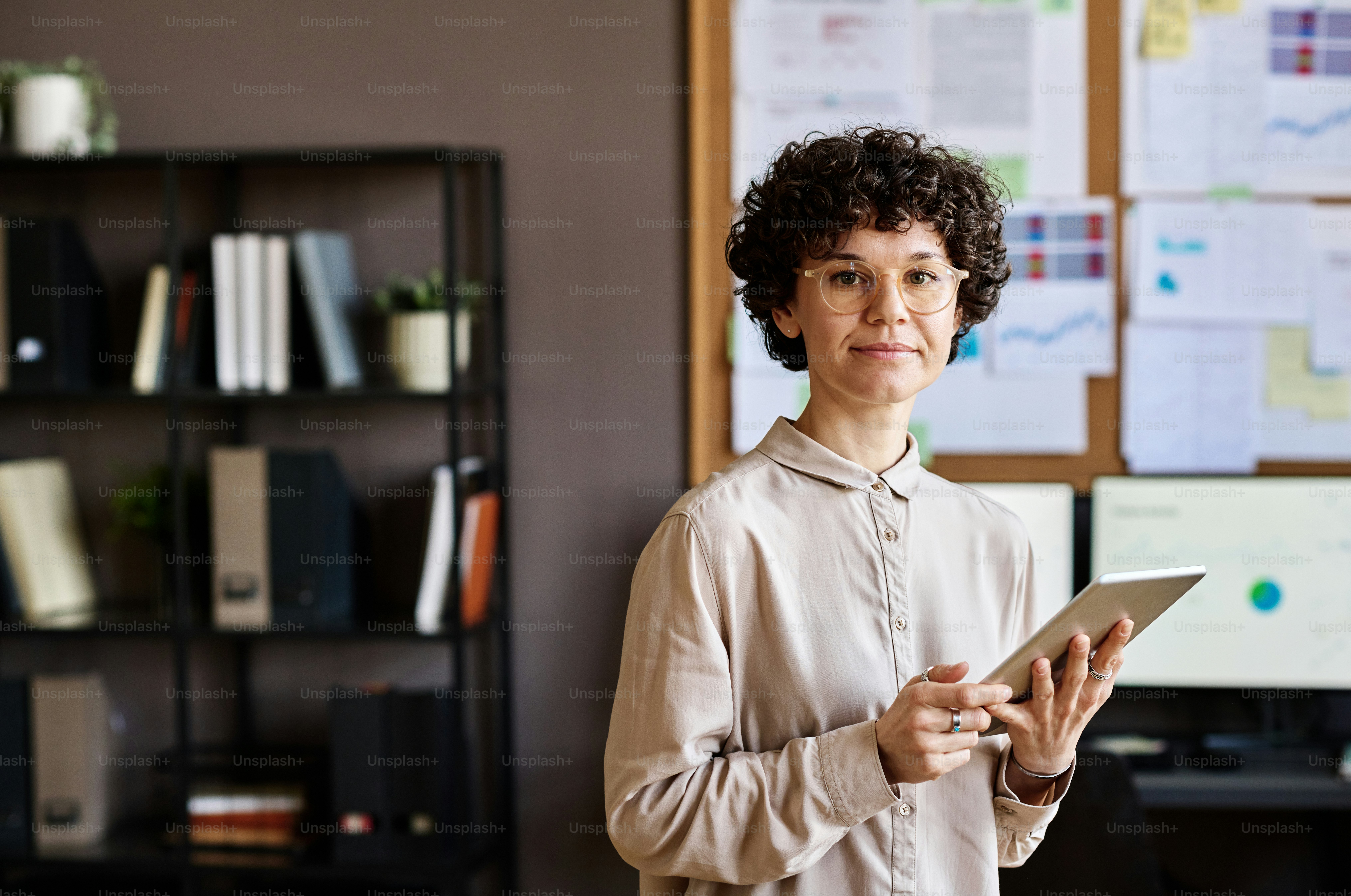 Portrait of young employee in eyeglasses looking at camera while using digital tablet at work