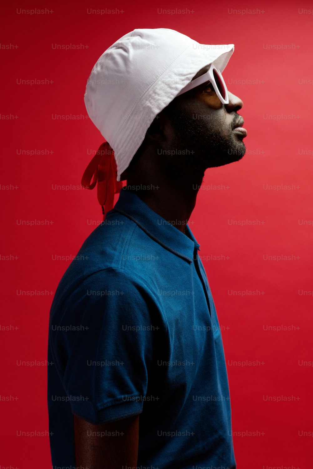 Retrato de perfil de moda de hombre negro con sombrero y gafas de sol sobre fondo rojo. Guapo modelo masculino afroamericano en elegante atuendo de verano en el estudio