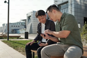 Dois jovens funcionários chineses assistindo vídeo on-line no smartphone do empresário em ambiente urbano