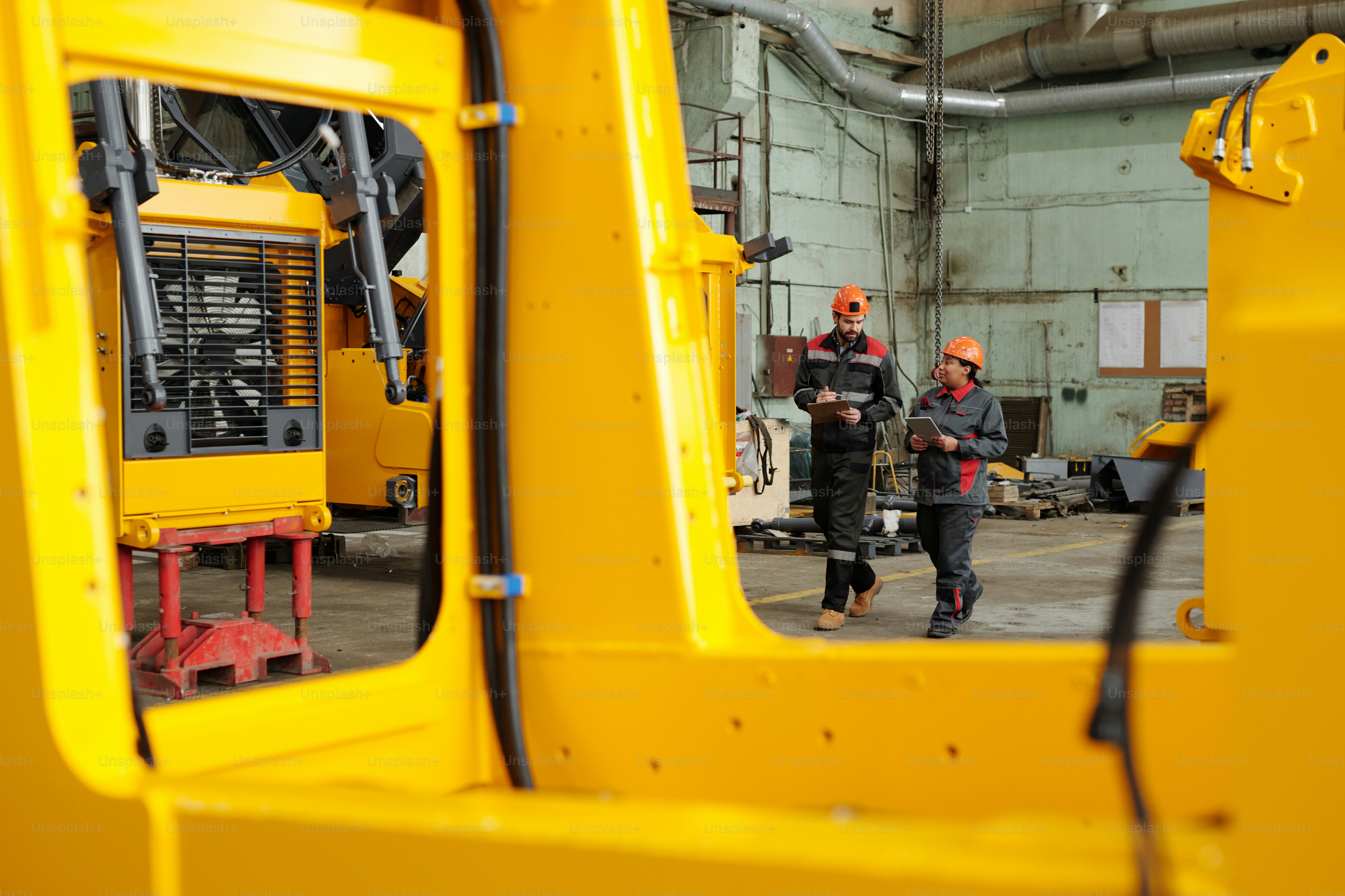 Dos jóvenes ingenieros con cascos y ropa de trabajo discutiendo mientras se desplazan por el taller de una gran planta industrial moderna