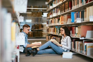 대학 도서관에서 공부하는 학생들. 책장 사이의 바닥에 앉아 책을 읽는 남자와 여자. 고해상도