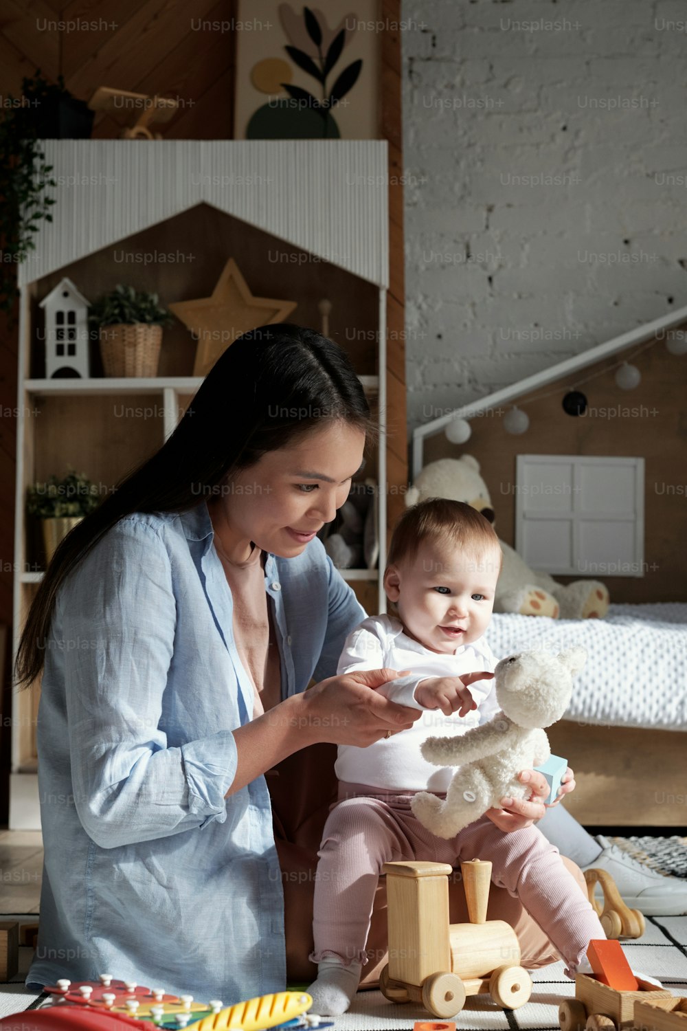 Foto vertical da jovem mãe moderna sentada no chão da sala de estar em casa brincando com sua filha bebê fofa