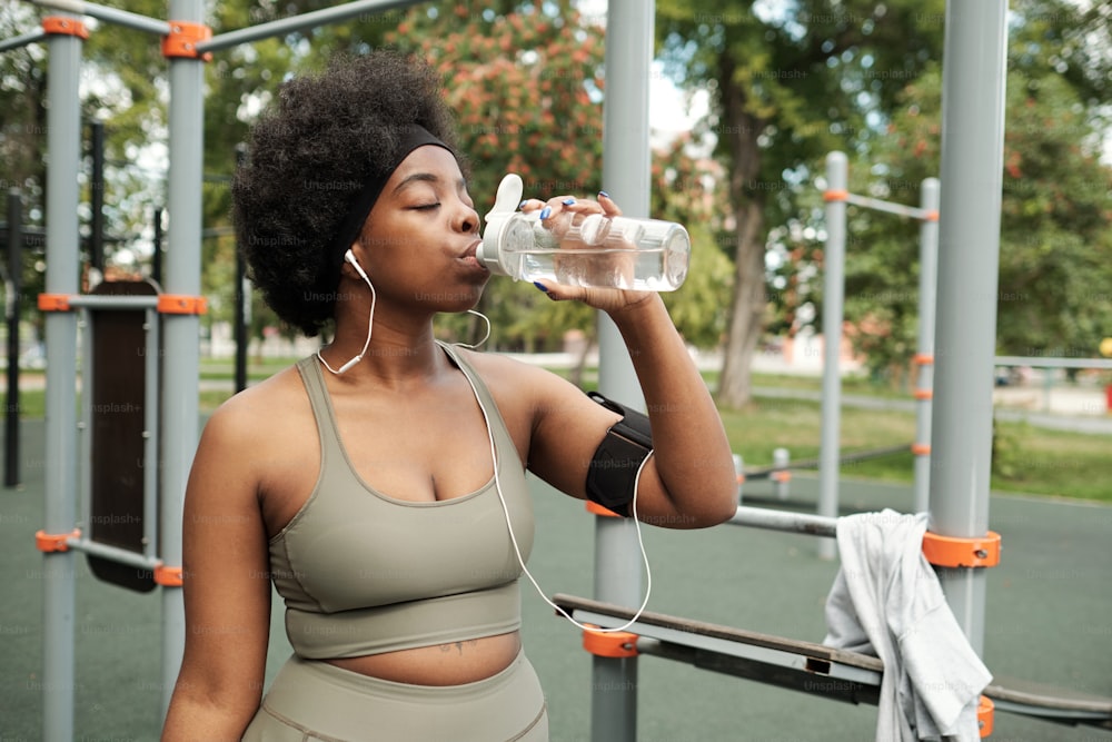 Thirsty sportswoman in tracksuit having water before continuing sports training