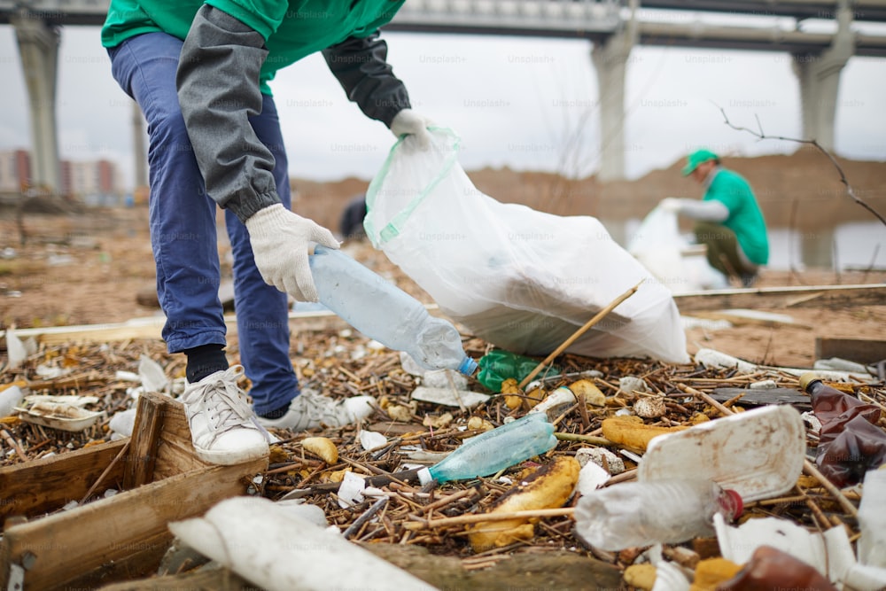 Lavoratore di un'azienda di protezione della natura che prende una bottiglia di plastica da un terreno imbevuto di rifiuti