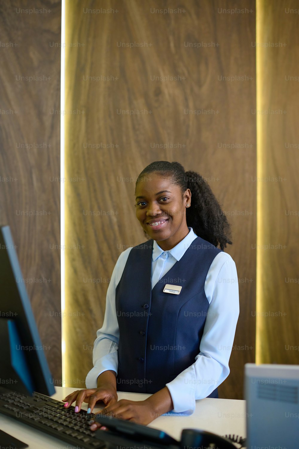 Young receptionist entering personal data of guests into database while standing in front of computer monitor by counter in hotel