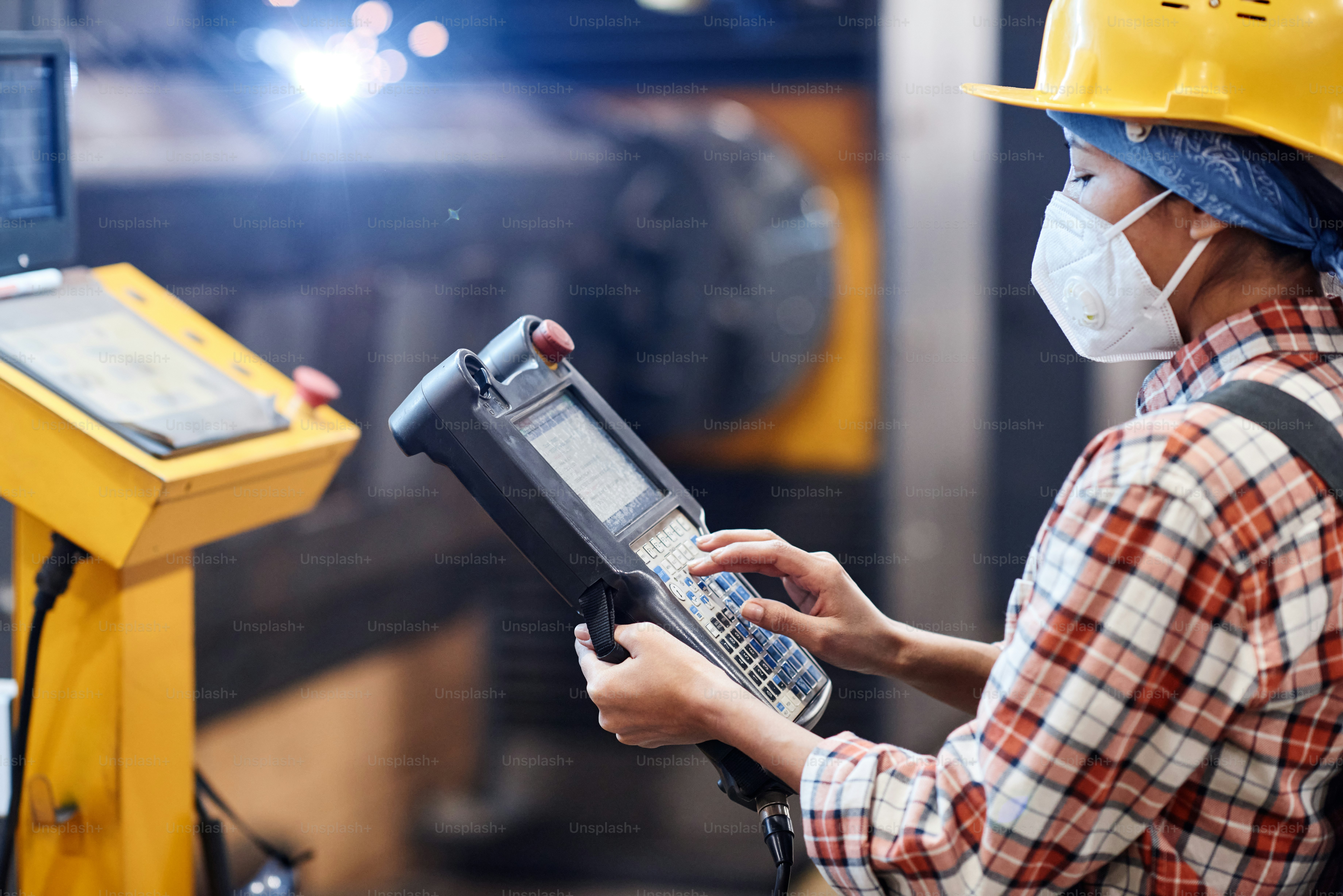 Female worker of plant in respirator and hardhat touching screen of switch device to control work of industrial machines