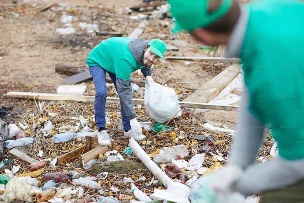 Worker of environmental protection company picking up non-recyclable trash from ground