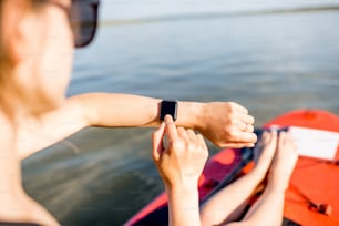 여름 방학 동안 호수에서 패들보딩을 하는 동안 스마트 시계를 사용하는 여자