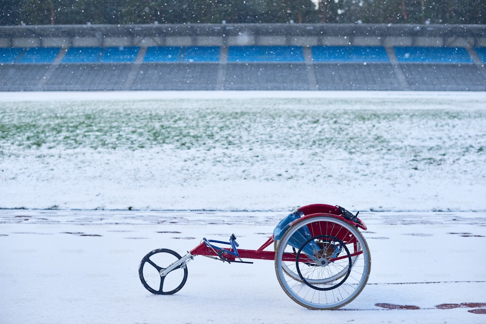 Silla de ruedas de carreras moderna de pie en el estadio de atletismo al aire libre cubierto de nieve en la sombría tarde de invierno