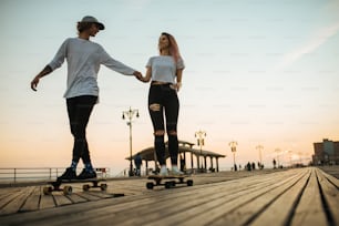 Silhouetten eines jungen Paares, das Longboards auf der Promenade draußen fährt
