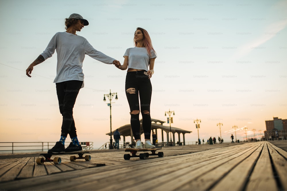 Silhouettes of young couple riding longboards on the boardwalk outside