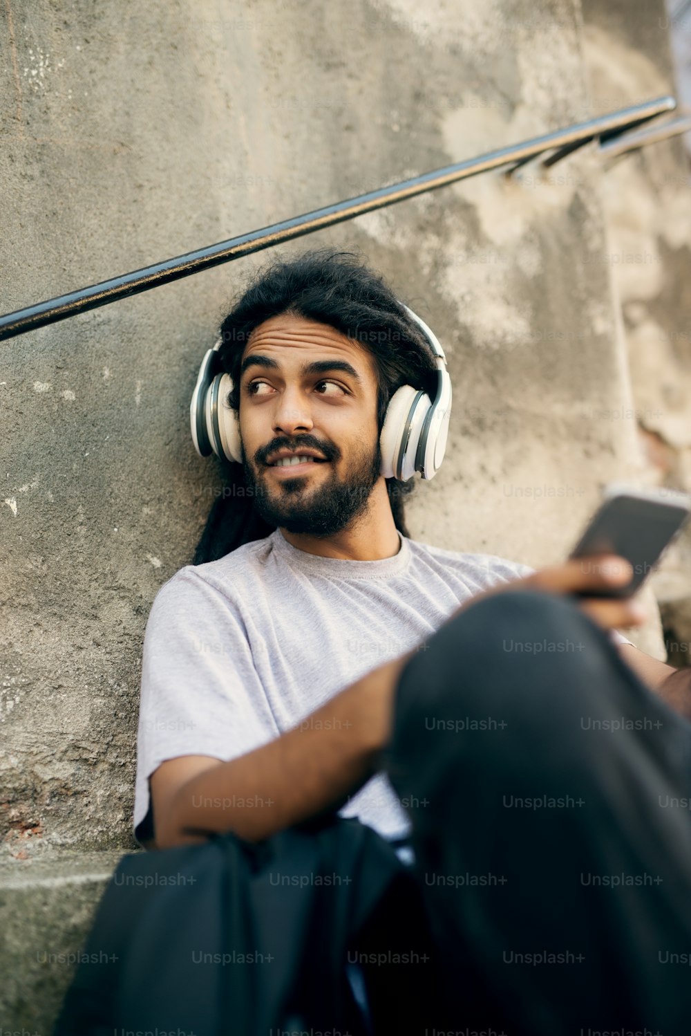 Casual young hipster with dreadlocks listening music at street and looking aside.