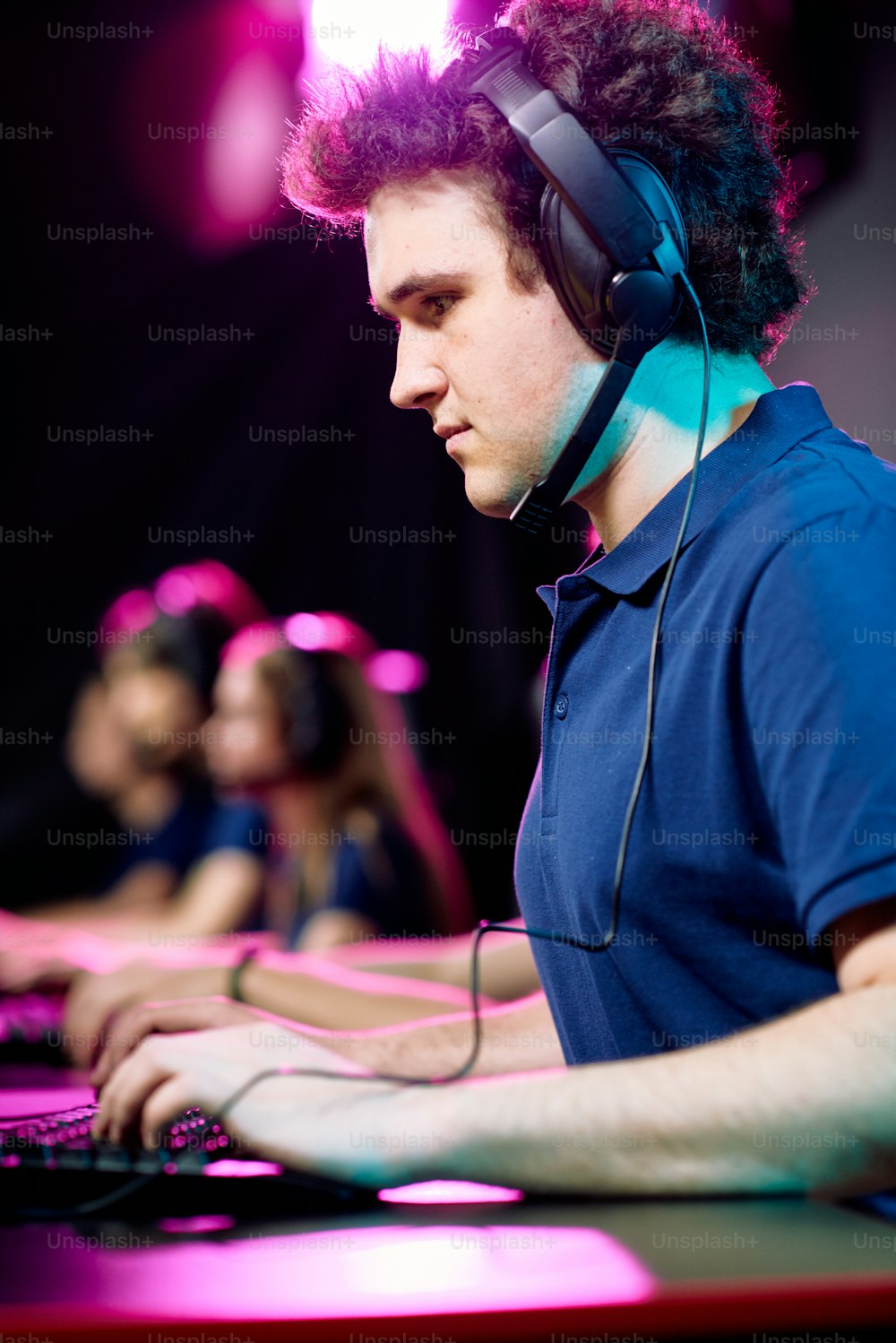 Ernsthafter junger Netzwerkspieler im Headset mit Mikrofon über Computertastatur beim Online-Spiel