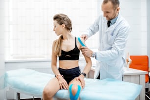 Senior therapist applying kinesio tape on a woman's shoulder during the medical treatment in the office