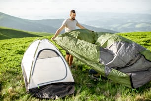 Man setting up the tent on the green meadow, traveling high in the mountains during the sunset