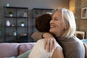 Happy senior woman embracing her friend while they standing in the room, they greeting each other during meeting