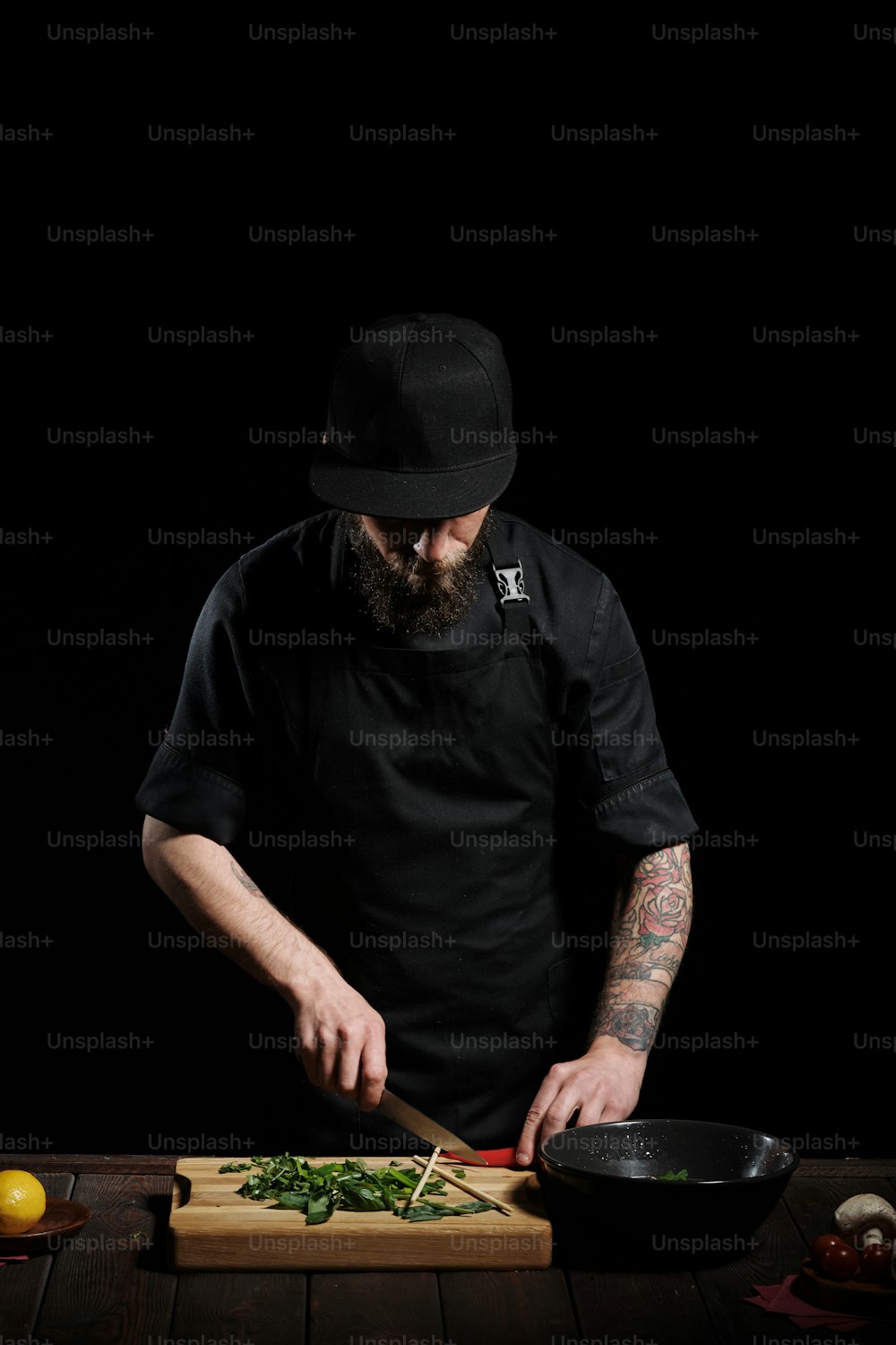 Ritratto di chef maschio che cucina pho bo in studio, tagliando peperoncino rosso piccante sulla tavola, su sfondo nero