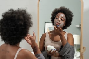 Young female applying mask on face in front of mirror in home environment