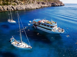 Aerial shot of beautiful blue lagoon at hot summer day with sailing boat. Top view of people are swimming around the boat.