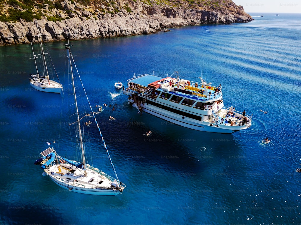 Aerial shot of beautiful blue lagoon at hot summer day with sailing boat. Top view of people are swimming around the boat.