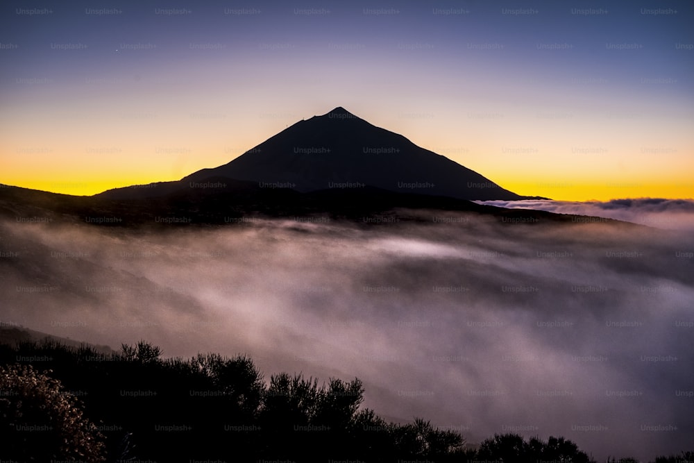 Wunderschöne El Teide Teneriffa Vulkanlandschaft mit hohem Gipfel und Wolken im Boden wie Nebel - zeitloser und Nationalpark malerischer Platz im Freien - farbiger Hintergrund und wilde Natur