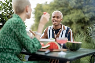 다인종 커플이 자연 위의 시골집 뒤뜰에서 저녁을 먹고 있다. 건강한 식생활과 현대적인 생활 방식에 대한 아이디어. 함께 시간을 즐기는 흑인 남성과 유럽 여성