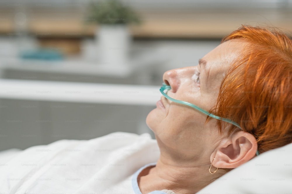 Close-up of elderly woman with tube in her nose to breath easily, she lying in bed at hospital ward