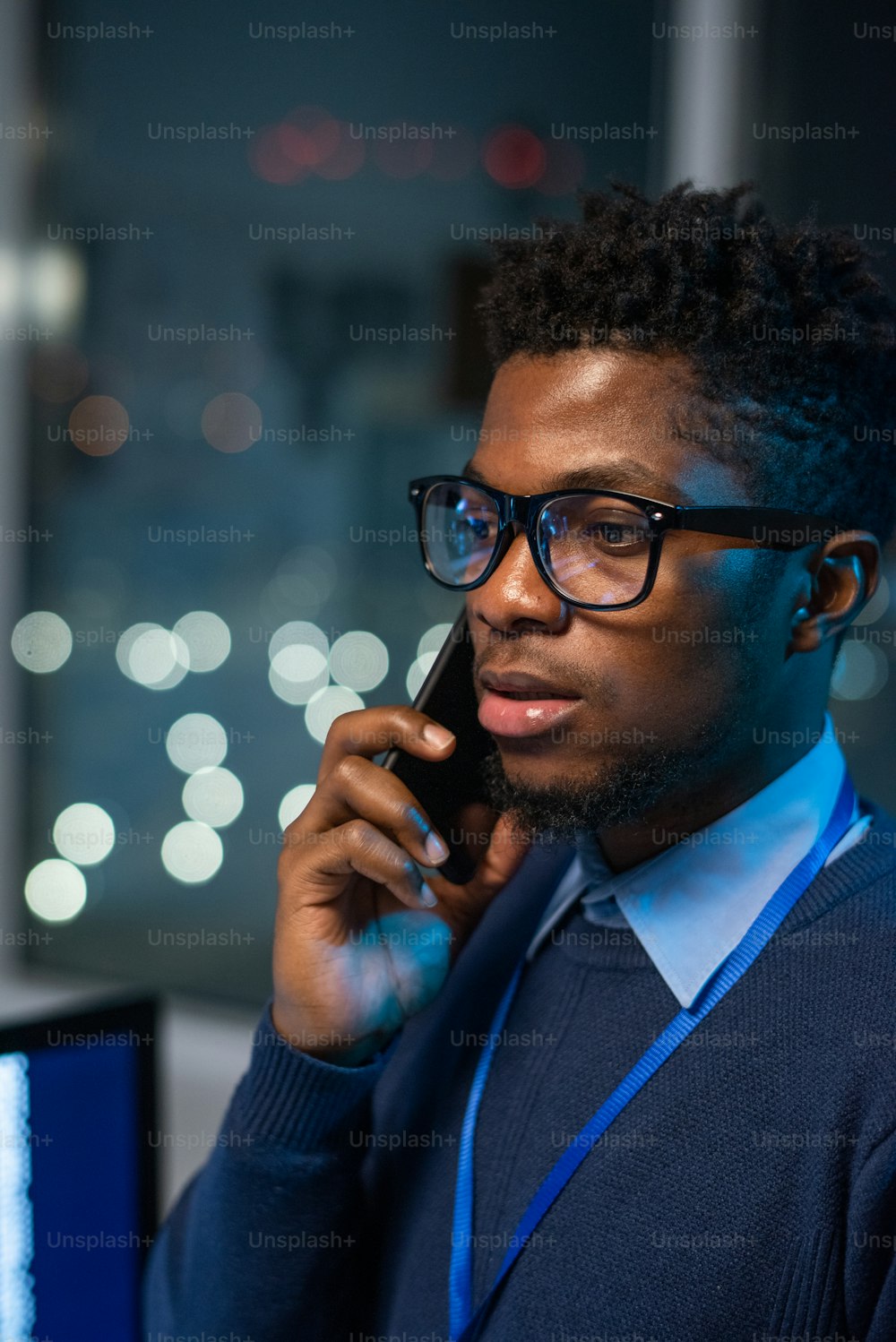スマートカジュアルウェアと眼鏡の若い自信に満ちたビジネスマンは、オフィス環境で携帯電話によるクライアントをコンサルティングします