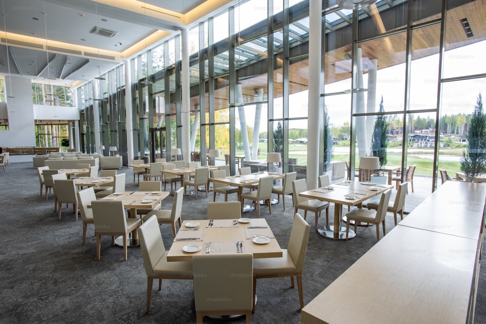 Two rows of tables served for guests in large luxurious restaurant of contemporary business center situated in natural environment