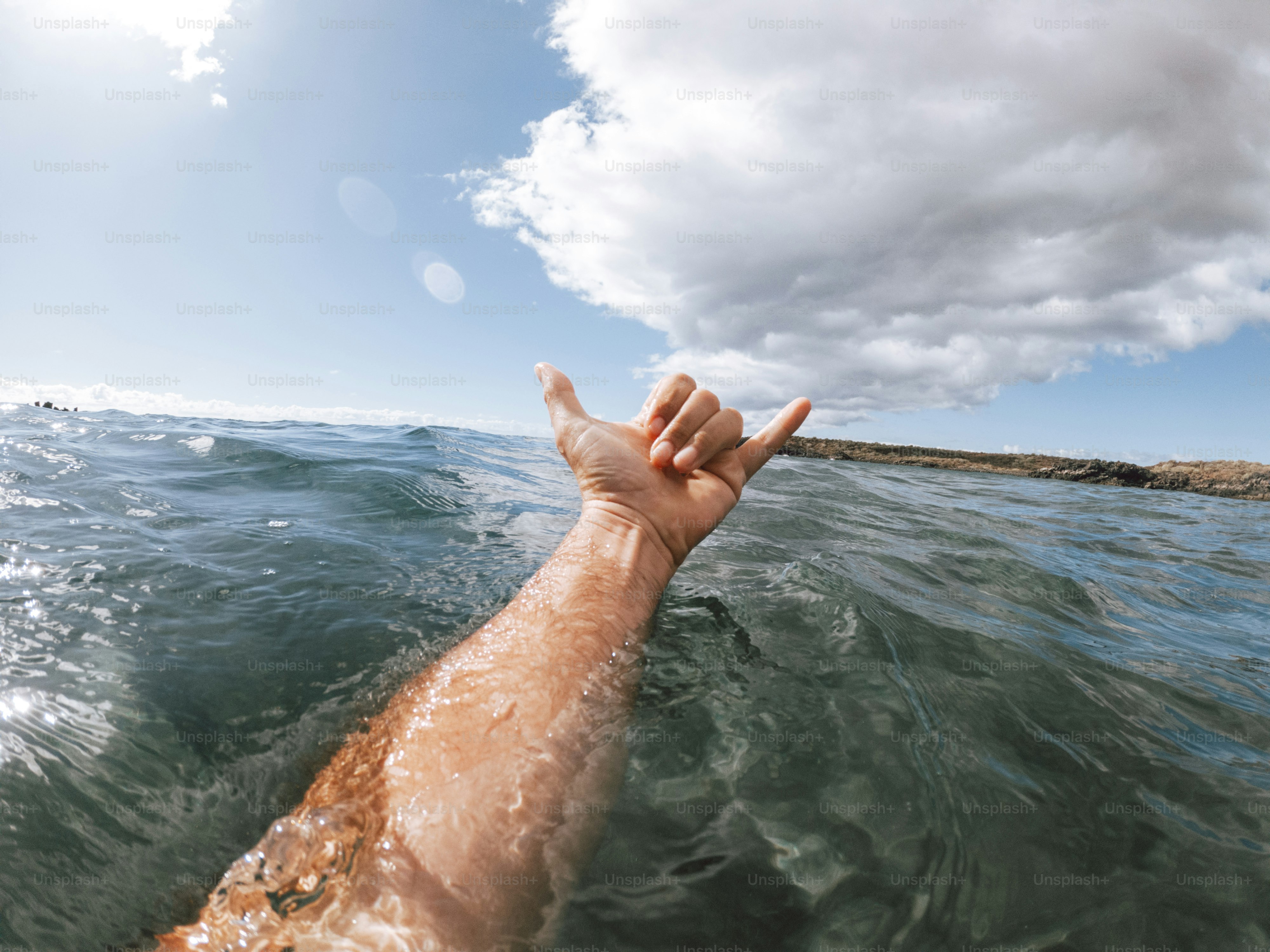 Man hands in surf sign hallo out of the blue ocean water with coast and nice sky in background - concept of people and summer holiday vacation