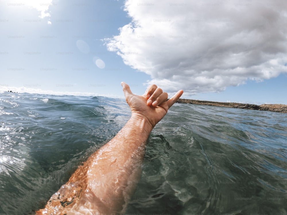 Man hands in surf sign hallo out of the blue ocean water with coast and nice sky in background - concept of people and summer holiday vacation