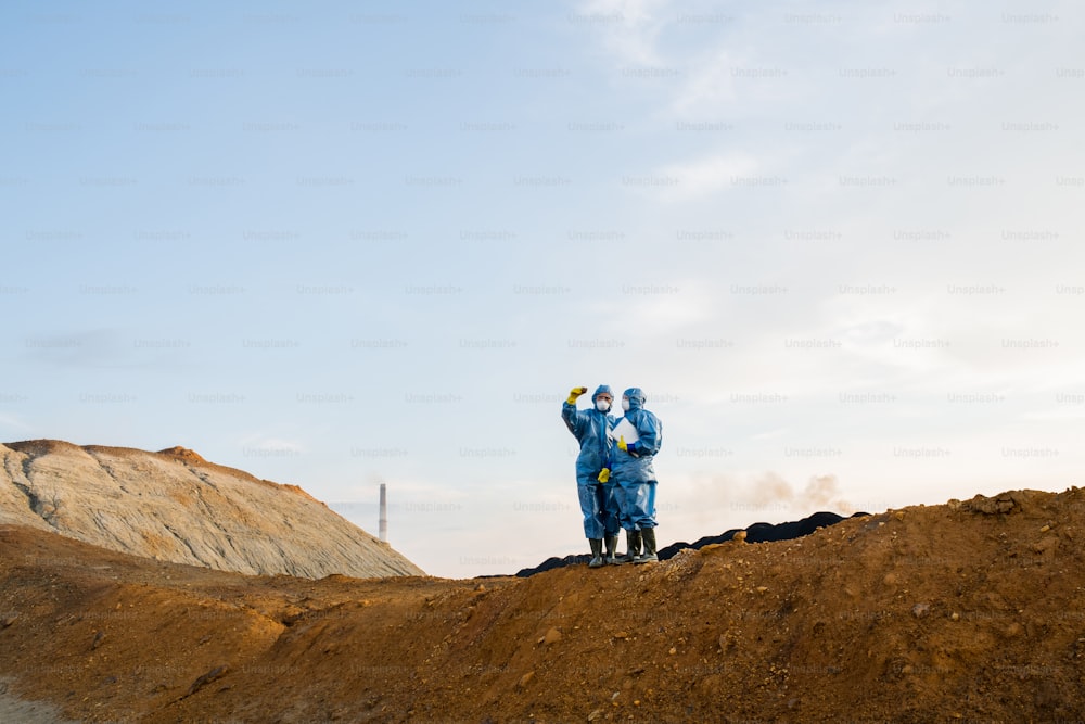 Piccole figure di due ecologisti in piedi sulla sommità di una collina durante l'indagine scientifica di un territorio abbandonato con suolo e aria inquinati