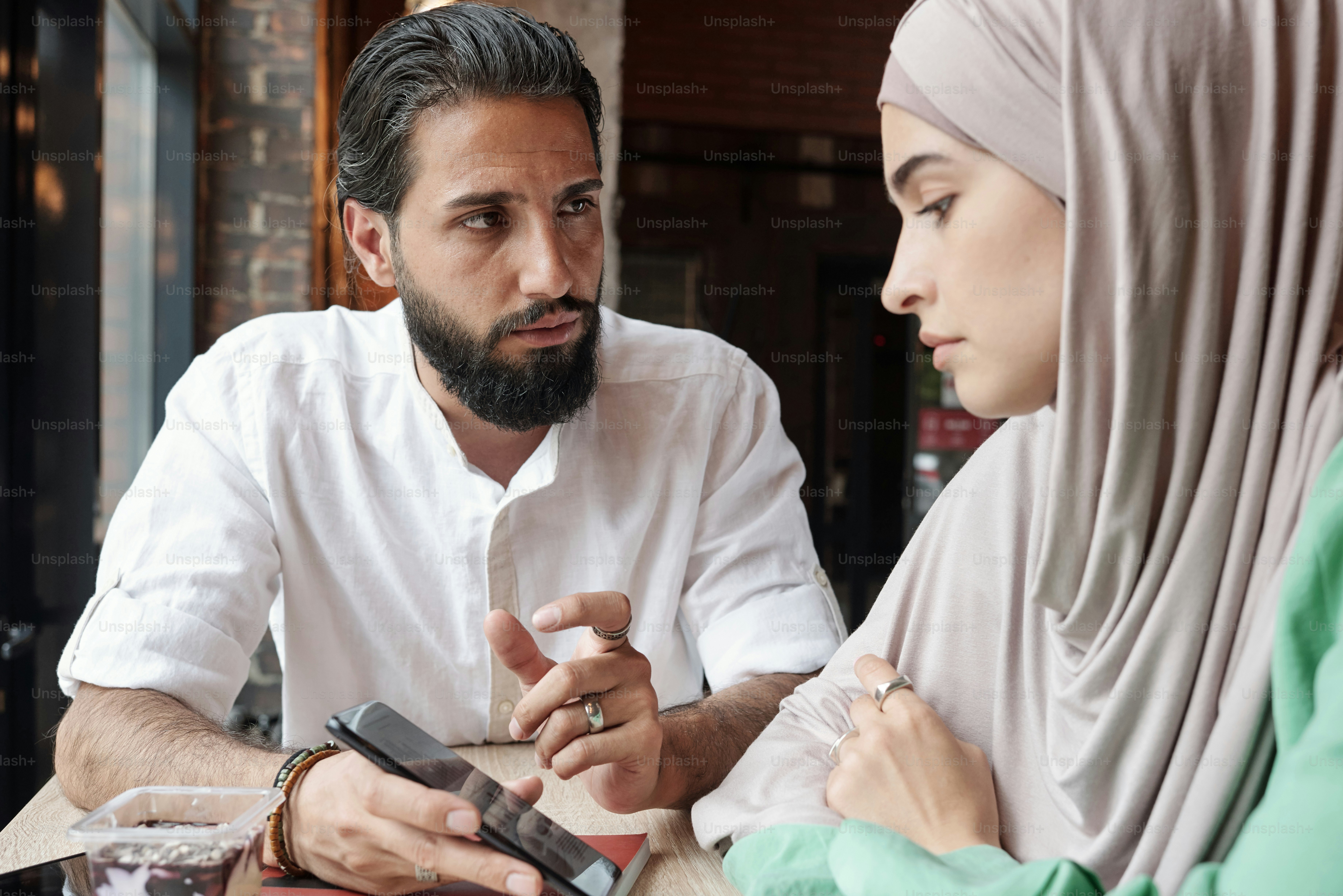 Un jeune homme musulman avec une barbe utilisant un téléphone tout en montrant un message sur les médias sociaux à une fille en hijab