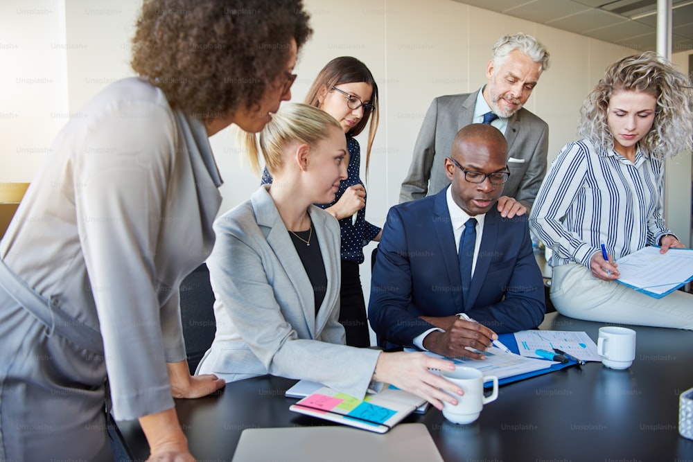 Diverse group of businesspeople reviewing paperwork together while having a meeting around a boardroom table in a modern office