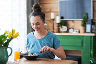 Mujer casual joven sentada junto a la mesa de la cena en la cocina mientras come espaguetis y bebe jugo de frutas