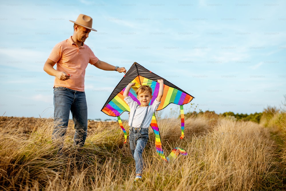 Pai com filho lançando pipa de ar colorida no campo. Conceito de uma família feliz se divertindo durante a atividade de verão
