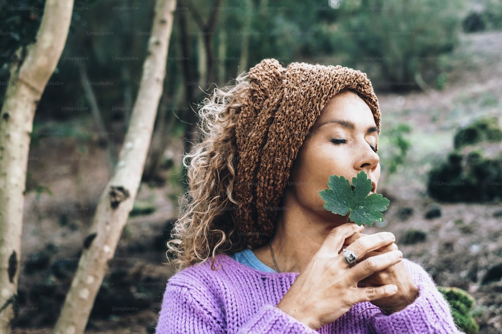 Pretty woman nature lover and inner life balance meditation lifestyle. Daydreaming female people holding green leaf in the forest with woods in background. Concept of human and earth feel