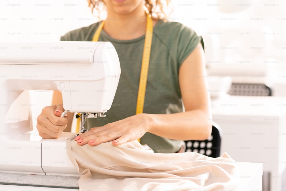 Professionelle Näherin sitzt an der Nähmaschine, während sie in der Werkstatt an einer neuen saisonalen Kollektion arbeitet