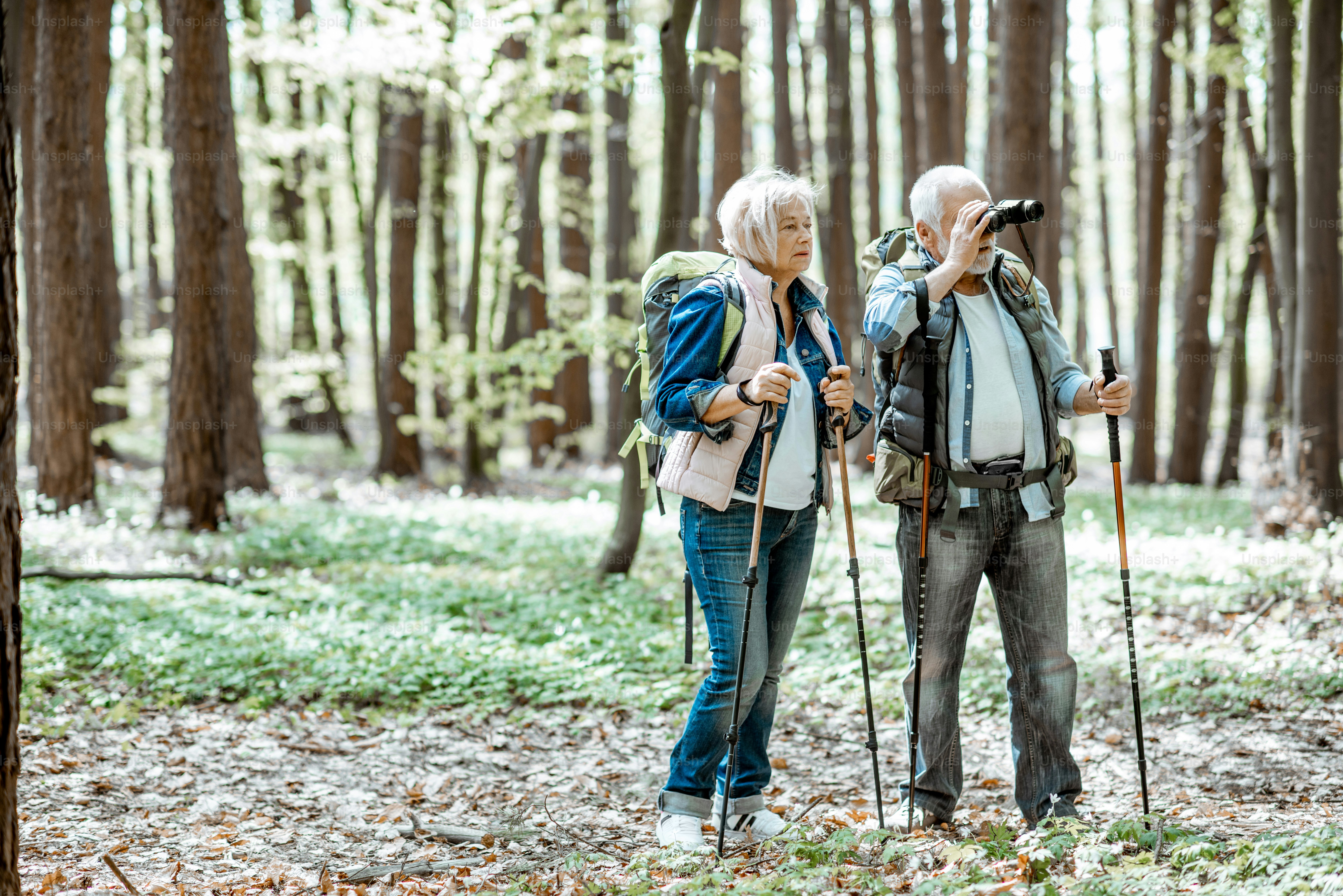 Senior couple looking with binoculars while hiking in the forest. Concept of an active lifestyle on retirement