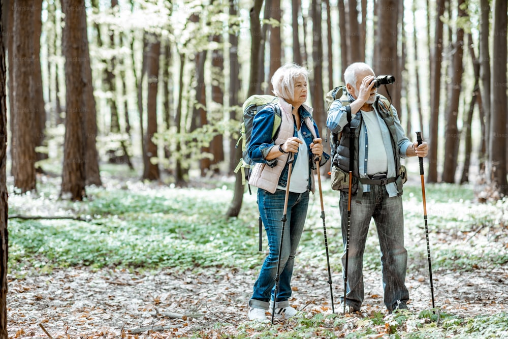 숲에서 하이킹을 하는 동안 쌍안경으로 보고 있는 노부부. 은퇴에 대한 활동적인 라이프 스타일의 개념