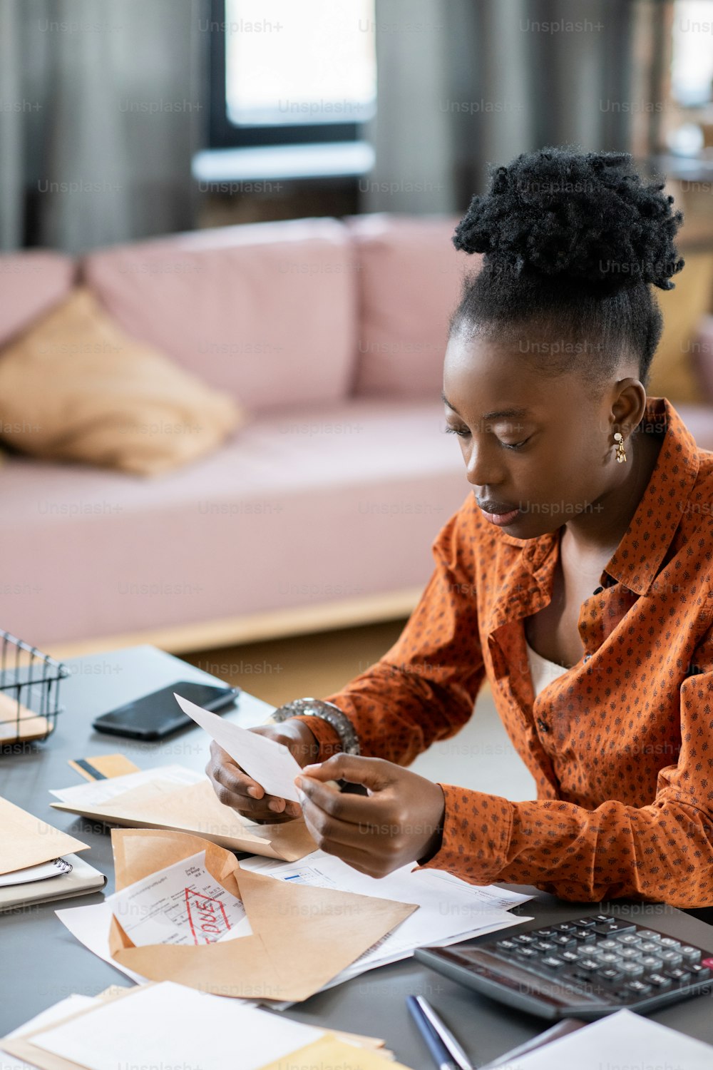 若いアフリカの女性は、書類と封印されていない封筒を持ってテーブルのそばに座りながら、財務書類や領収書を見ています